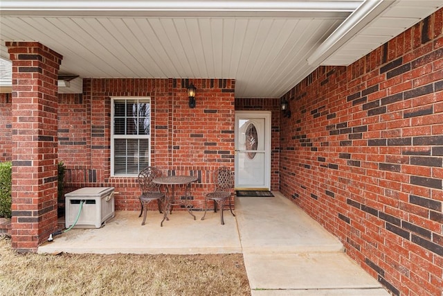 view of exterior entry featuring brick siding and a patio area