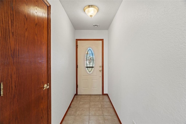 doorway to outside with light tile patterned floors, a textured wall, a textured ceiling, visible vents, and baseboards