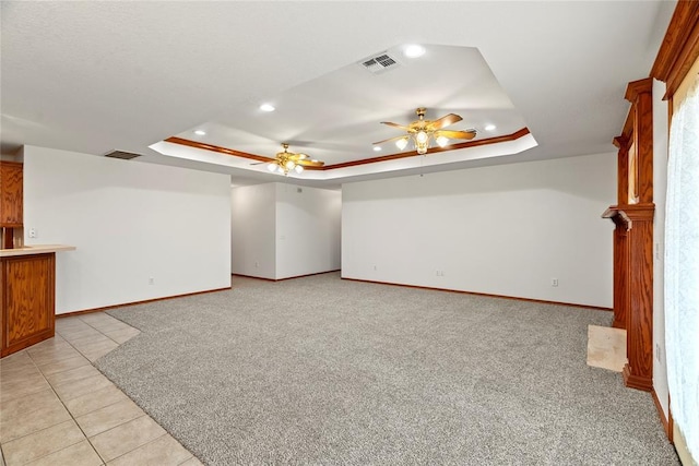 unfurnished living room featuring light carpet, visible vents, a tray ceiling, and a ceiling fan