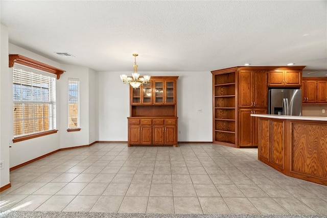 interior space with a notable chandelier, visible vents, stainless steel refrigerator with ice dispenser, brown cabinets, and open shelves