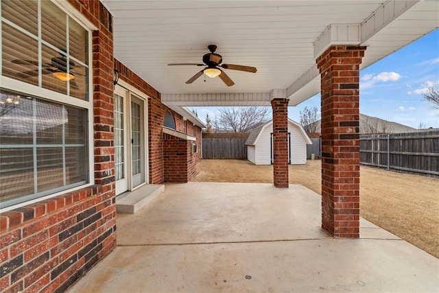 view of patio / terrace with a fenced backyard, ceiling fan, an outdoor structure, and a storage shed