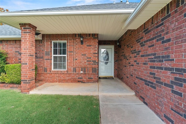 501 N Cherokee Way, Mustang, OK 73064 - view of exterior entry with brick siding, roof with shingles, and a patio area