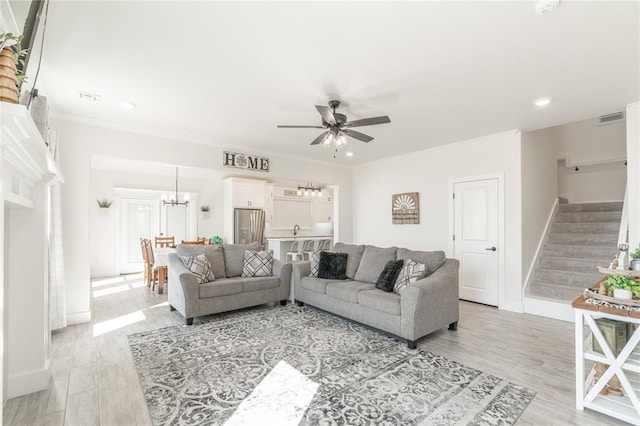 living room featuring stairs, visible vents, crown molding, and ceiling fan with notable chandelier