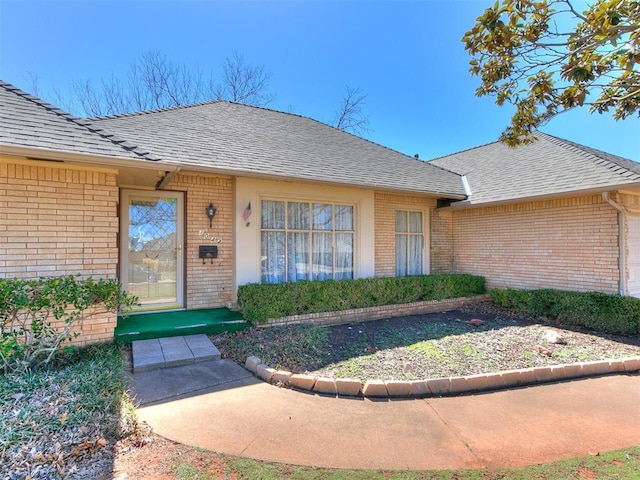 doorway to property with a shingled roof and brick siding