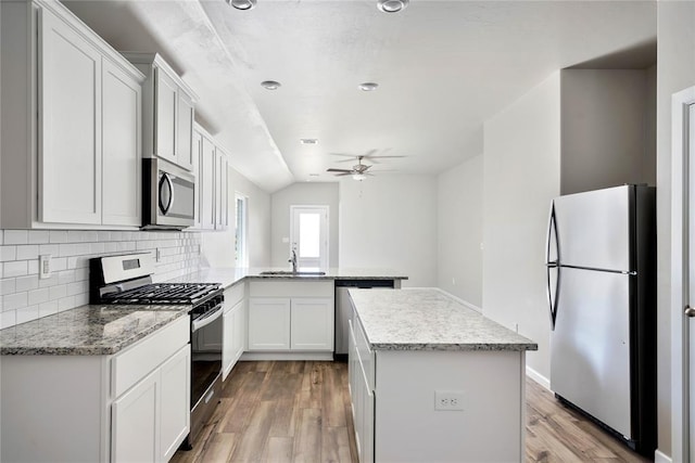 kitchen with appliances with stainless steel finishes, light wood-style floors, a peninsula, and a kitchen island