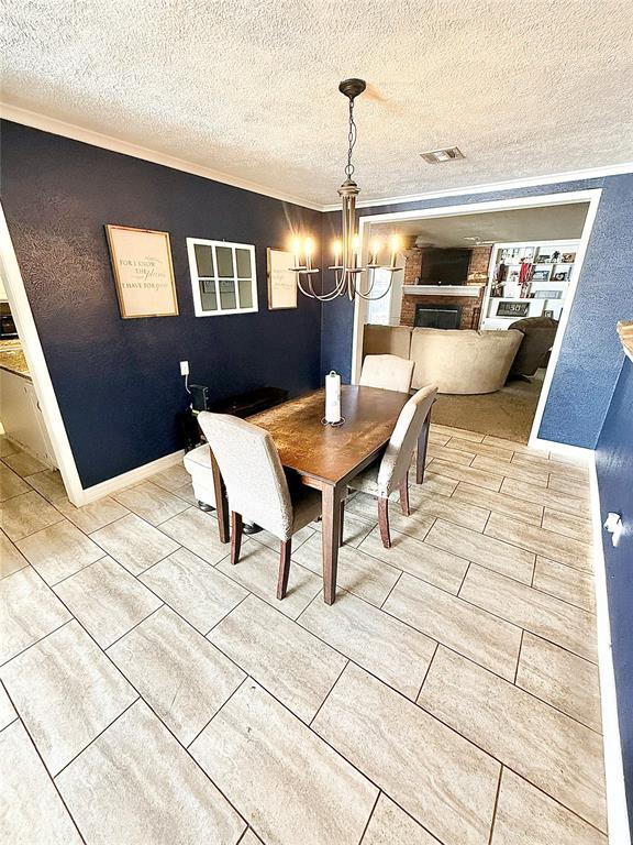 unfurnished dining area featuring a fireplace, visible vents, an inviting chandelier, ornamental molding, and a textured ceiling