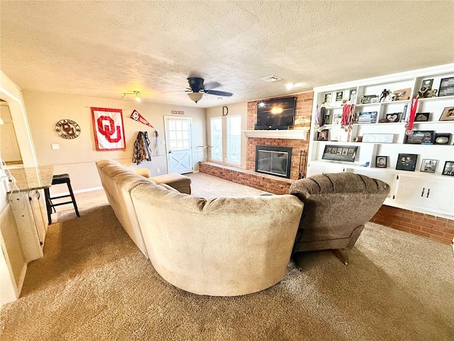 living room featuring a brick fireplace, a textured ceiling, visible vents, and carpet flooring