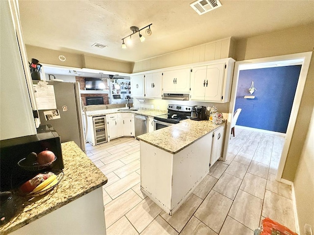 kitchen with under cabinet range hood, a peninsula, visible vents, white cabinets, and appliances with stainless steel finishes