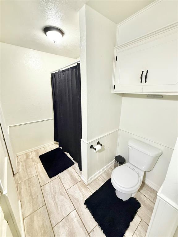 bathroom with toilet, wood tiled floor, a decorative wall, and a shower with shower curtain