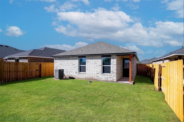 rear view of house with a fenced backyard, roof with shingles, a lawn, and brick siding