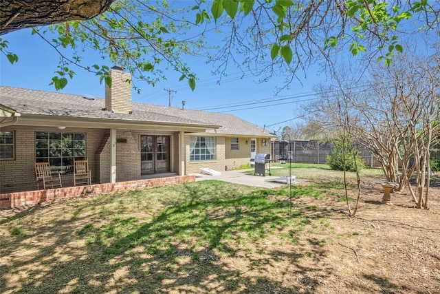 back of house featuring a lawn, a patio, fence, brick siding, and a chimney