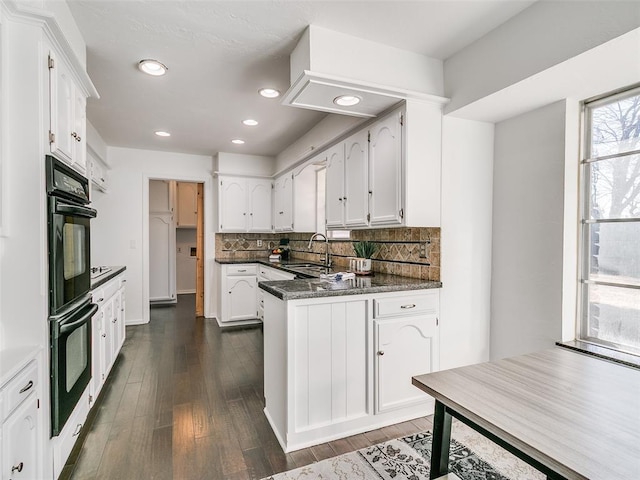 kitchen with dark countertops, a peninsula, white cabinetry, dobule oven black, and a sink