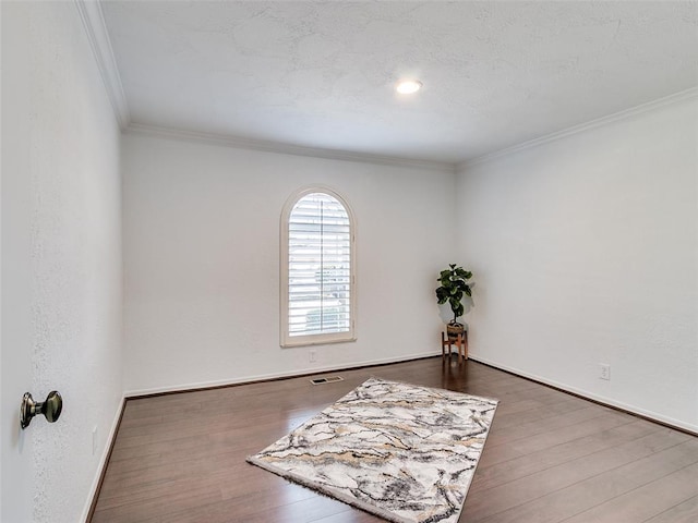 empty room featuring wood finished floors, baseboards, visible vents, ornamental molding, and a textured ceiling