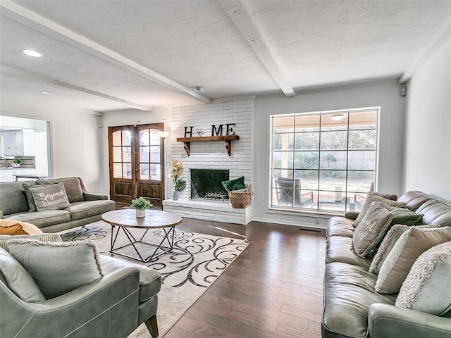 living room featuring beam ceiling, a fireplace, a textured ceiling, and wood finished floors