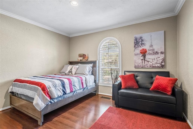 bedroom featuring wood finished floors, visible vents, and a textured wall