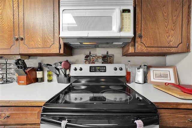 kitchen featuring electric range, light countertops, white microwave, and brown cabinets