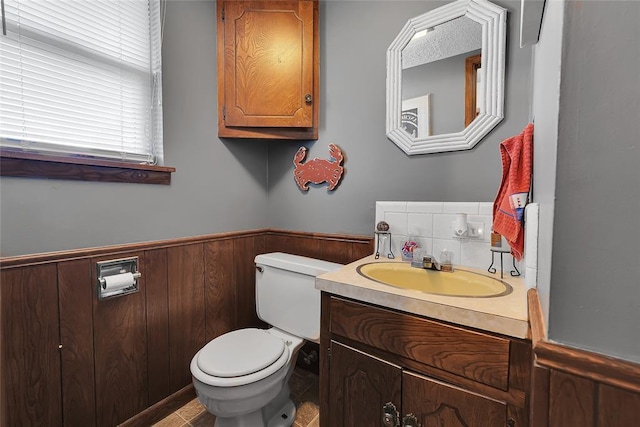 half bath with wainscoting, vanity, toilet, and wooden walls