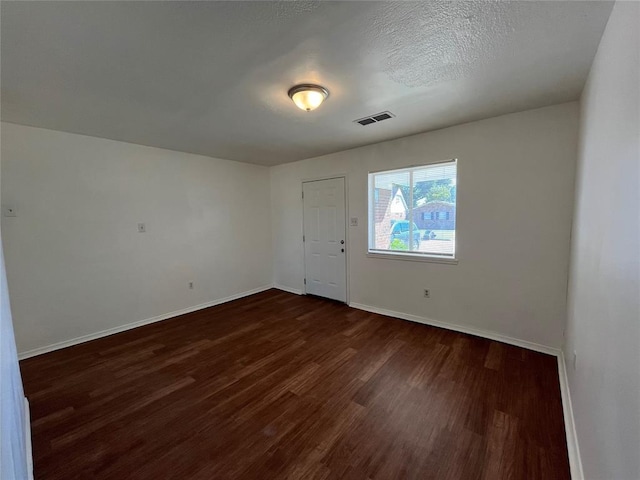 empty room with a textured ceiling, dark wood-style flooring, visible vents, and baseboards