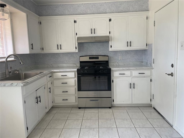 kitchen featuring tasteful backsplash, light countertops, under cabinet range hood, a sink, and gas stove