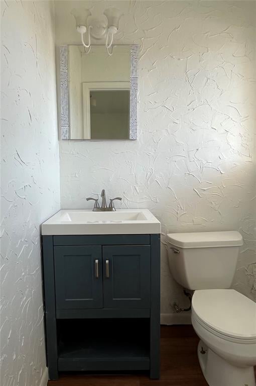 half bath featuring a textured wall, vanity, and toilet