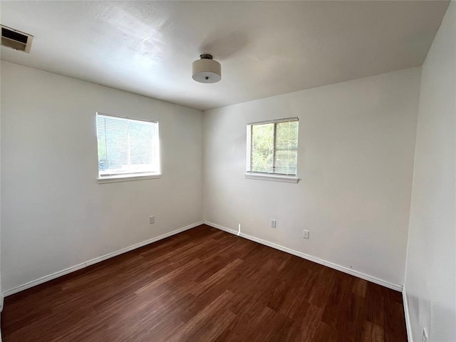 spare room featuring visible vents, baseboards, and dark wood-type flooring