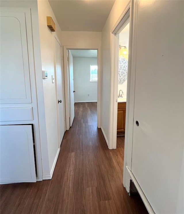 corridor featuring dark wood-style flooring and baseboards