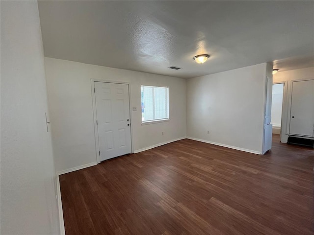 empty room featuring dark wood finished floors, visible vents, and baseboards