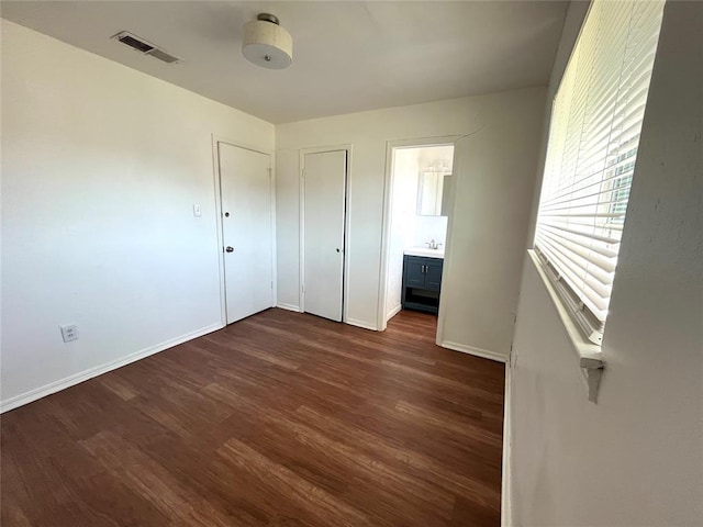 unfurnished bedroom with ensuite bath, baseboards, visible vents, and dark wood-type flooring