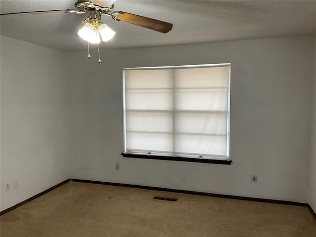 carpeted spare room featuring baseboards, visible vents, and a ceiling fan