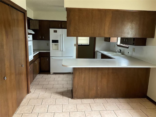 kitchen featuring light countertops, a sink, dark brown cabinets, white appliances, and a peninsula