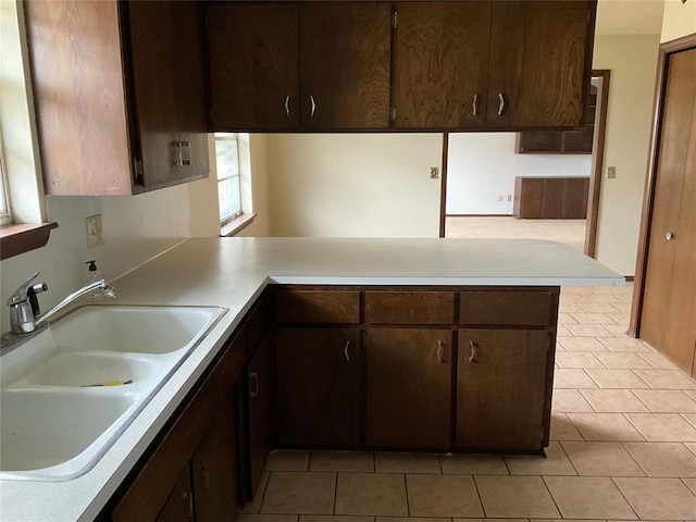 kitchen with light tile patterned floors, a peninsula, light countertops, dark brown cabinets, and a sink