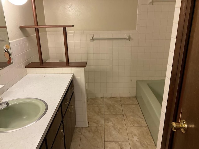 full bathroom featuring tile patterned flooring, vanity, tile walls, wainscoting, and a bathtub