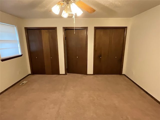 unfurnished bedroom with a ceiling fan, baseboards, visible vents, multiple closets, and carpet