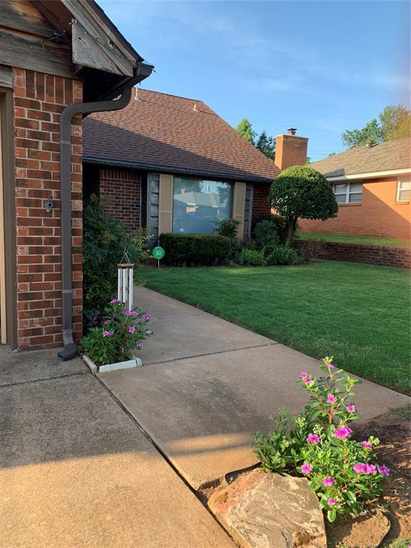 view of exterior entry featuring a shingled roof, brick siding, a yard, and a chimney