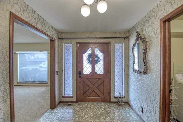 carpeted foyer featuring a chandelier and baseboards