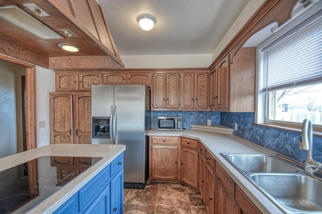 kitchen featuring brown cabinetry, appliances with stainless steel finishes, a sink, light countertops, and backsplash