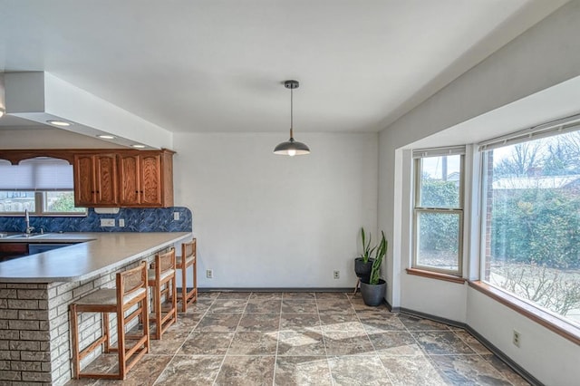 kitchen with stone finish floor, brown cabinets, baseboards, and a healthy amount of sunlight