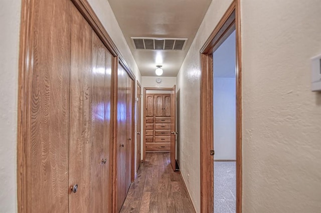 hall featuring visible vents, wood finished floors, and a textured wall