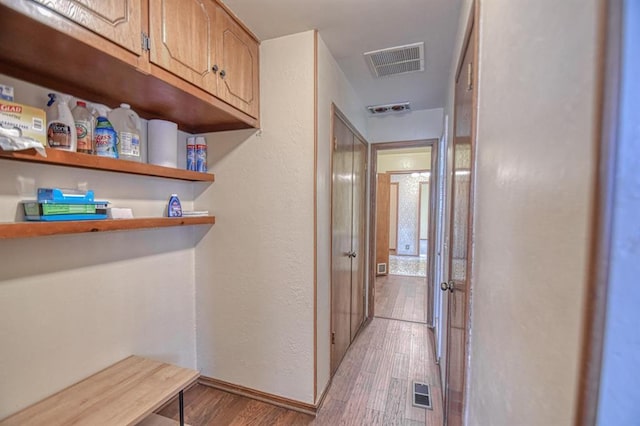 hallway featuring baseboards, visible vents, wood finished floors, and a textured wall