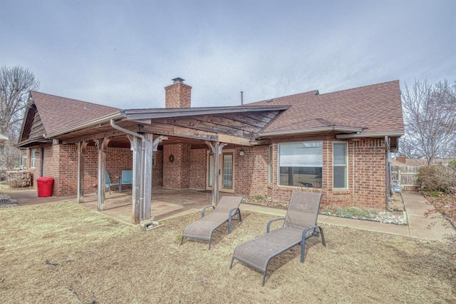 rear view of property with roof with shingles, brick siding, a chimney, and a patio area