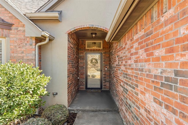 property entrance with stucco siding, brick siding, and roof with shingles