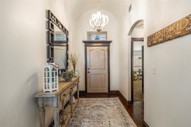 foyer entrance featuring a chandelier, visible vents, baseboards, vaulted ceiling, and dark wood-style floors