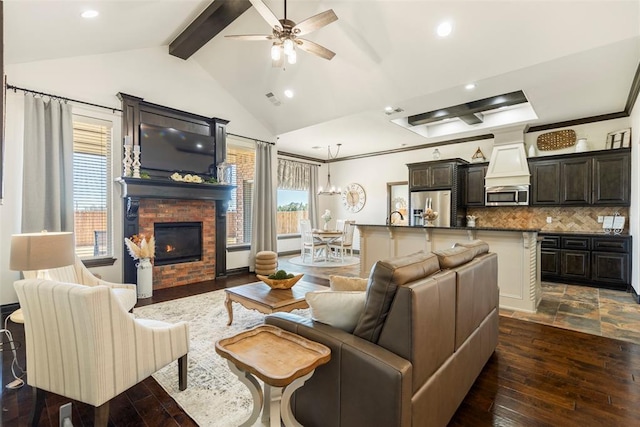 living area with a ceiling fan, a glass covered fireplace, beamed ceiling, dark wood-type flooring, and recessed lighting