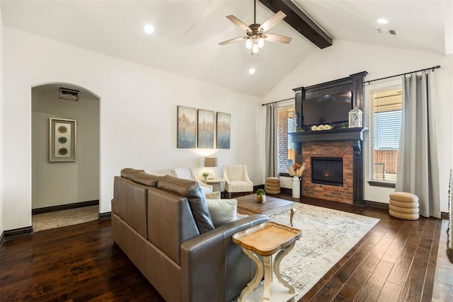 living area featuring arched walkways, visible vents, lofted ceiling with beams, dark wood-type flooring, and a lit fireplace