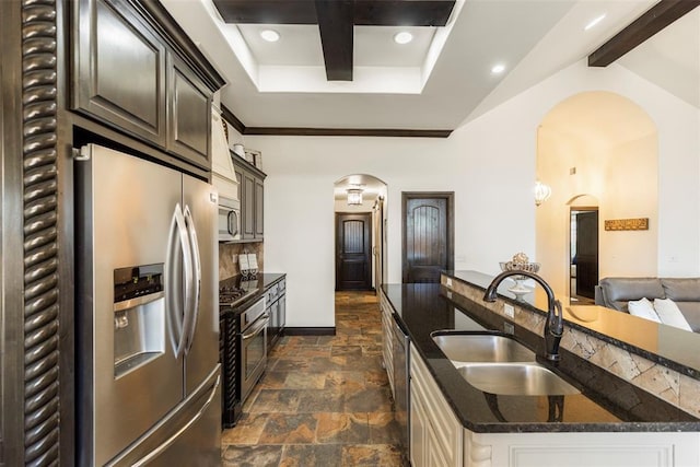 kitchen with arched walkways, a sink, appliances with stainless steel finishes, stone finish flooring, and beamed ceiling