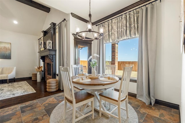 dining space with a glass covered fireplace, stone tile flooring, baseboards, and an inviting chandelier