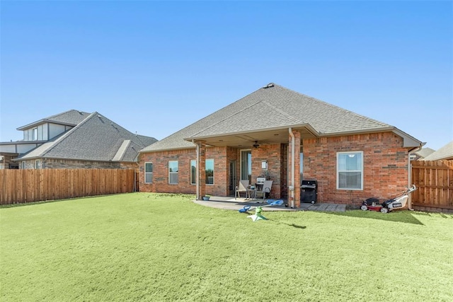 back of property with a lawn, a ceiling fan, a fenced backyard, a patio area, and brick siding