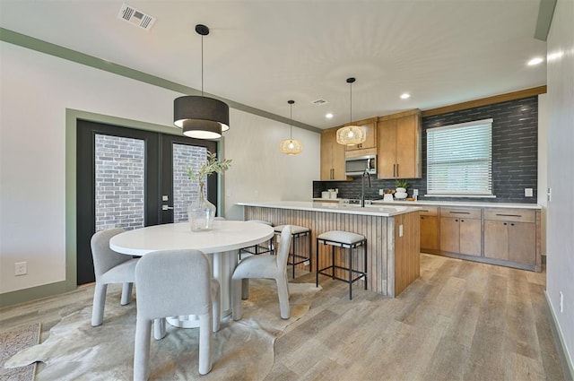 kitchen with light countertops, stainless steel microwave, backsplash, visible vents, and light wood-type flooring