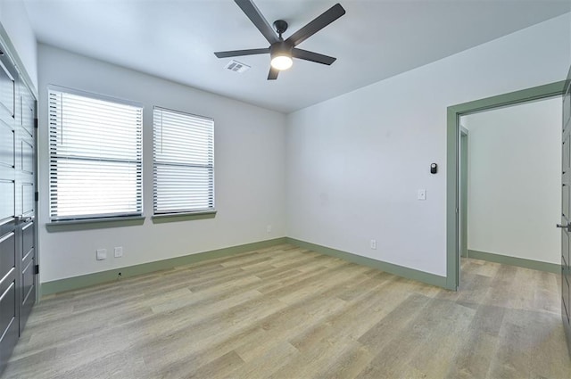 empty room with light wood finished floors, a ceiling fan, visible vents, and baseboards