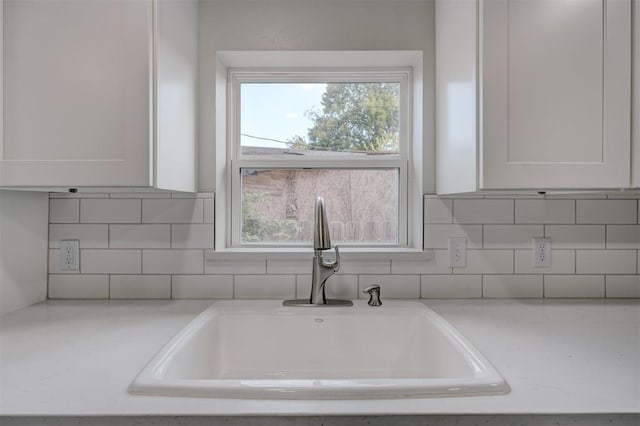 kitchen with tasteful backsplash, white cabinetry, a sink, and light stone countertops